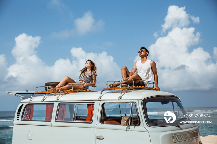 young couple with sunglasses sitting on top of minivan roof