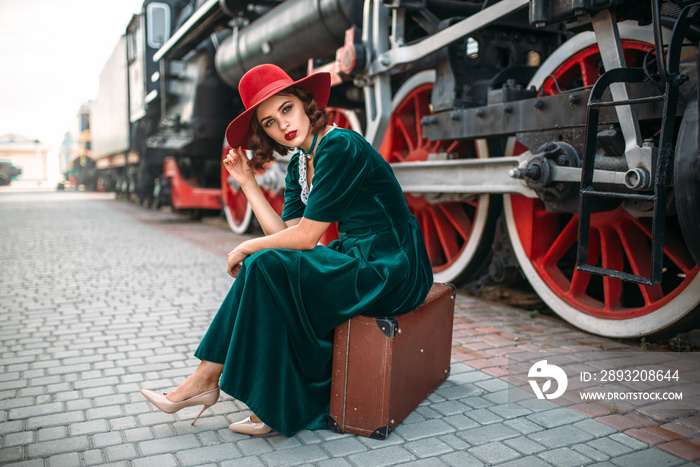 坐在行李箱上靠着蒸汽火车的女人