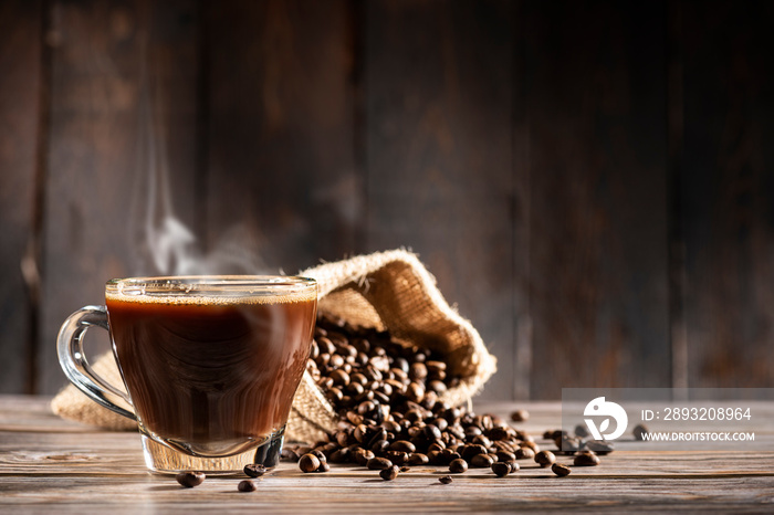 glass cup full of steamed coffee on wooden background with coffee beans