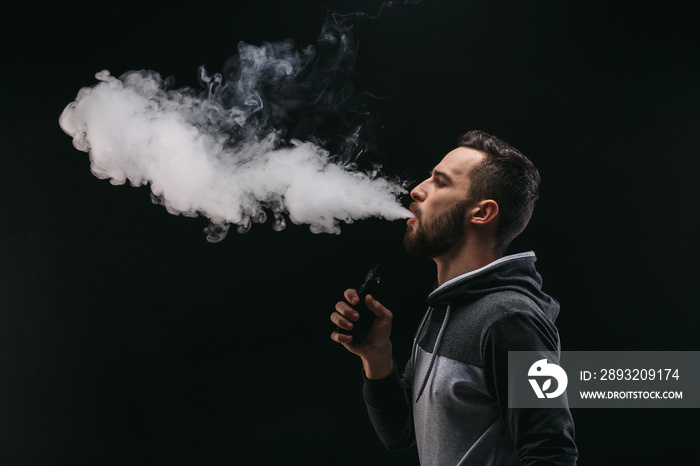 Young man vaping e-cigarette with smoke on black