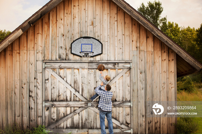 Father and son playing basketball in front of wooden barn