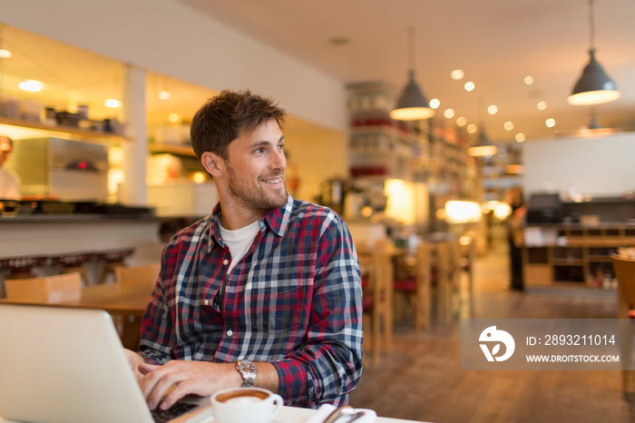 Smiling man working at laptop in cafe