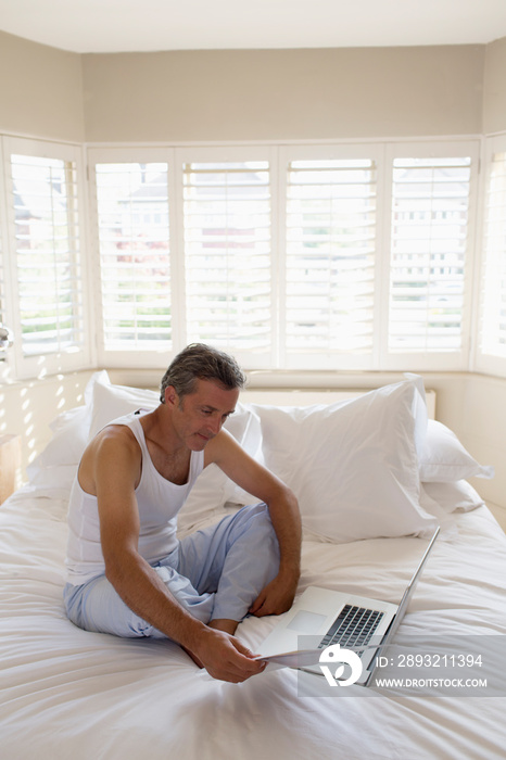 Man in pajamas working at laptop on bed