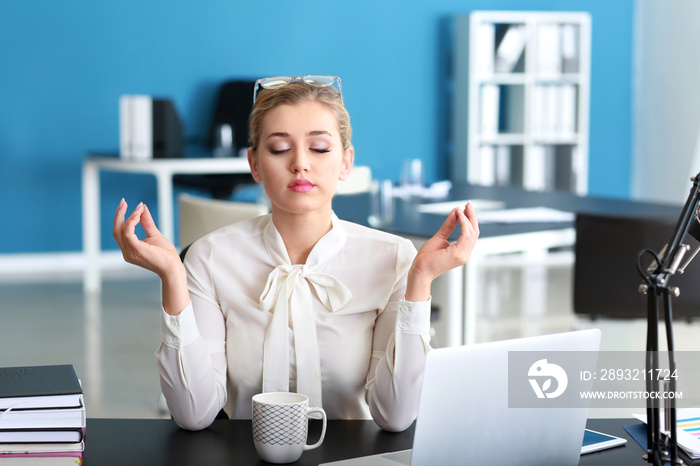 Beautiful businesswoman meditating at table in office