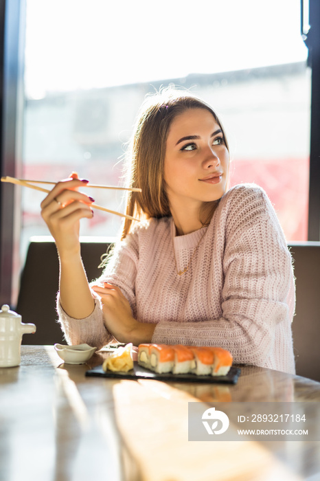 Beautiful young girl enjoying sushi in a cafe on a sunny day