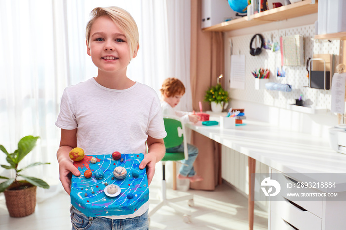 happy young school kid, boy showing the model of solar system made from plasticine, kids room backgr