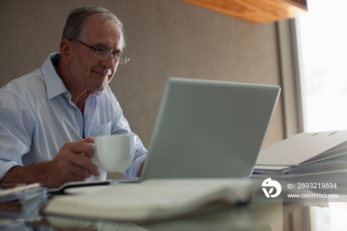 Smiling senior man with coffee working at laptop