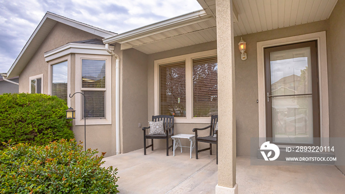 Panorama Chairs and table at the concrete porch of a home with bay windows at the facade