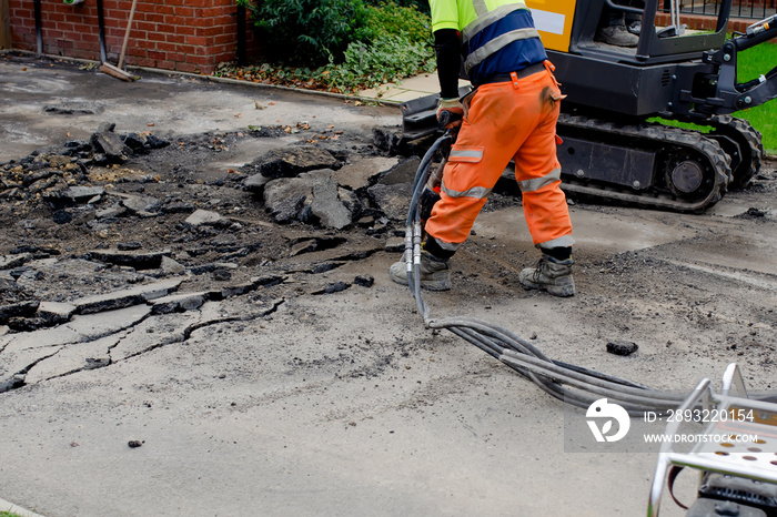 Construction worker breaking road gully using hydraulic breacker during road works on new housing de