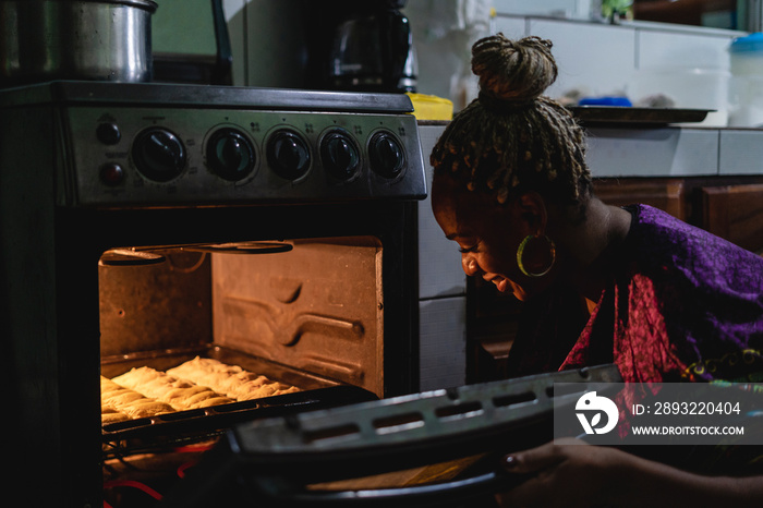 Imagen horizontal de una mujer afrocaribeña en el interior de su cocina sacando del horno unos bocad