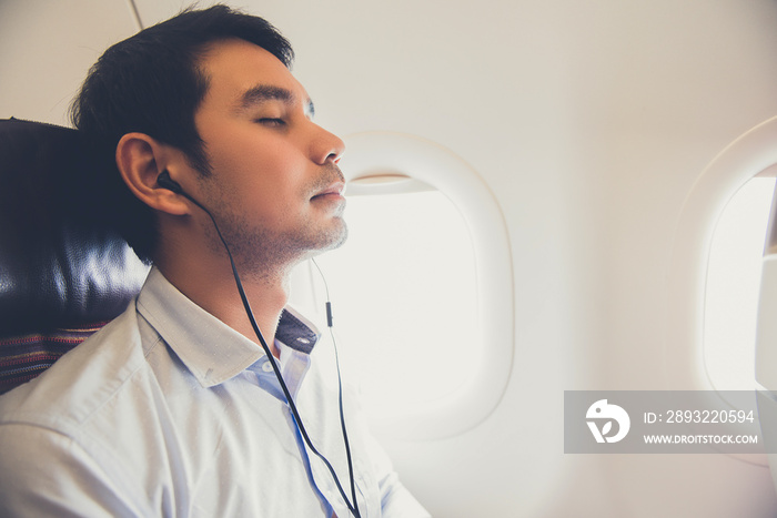 睡觉的男乘客戴着耳机在飞机上听音乐