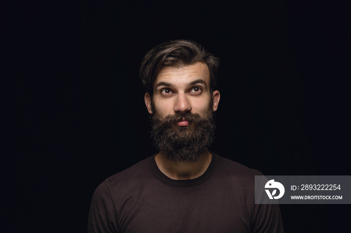 Close up portrait of young man isolated on black studio background. Photoshot of real emotions of ma