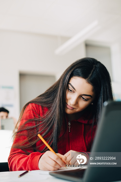 Teenage girl with long hair writing in book while studying at university