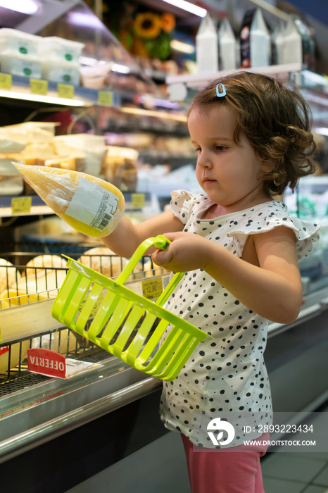 小女孩在超市买奶酪。孩子在展示柜前拿着小篮子。