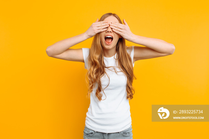 beautiful girl closes her eyes with her hands, on a yellow background, playing hide and seek