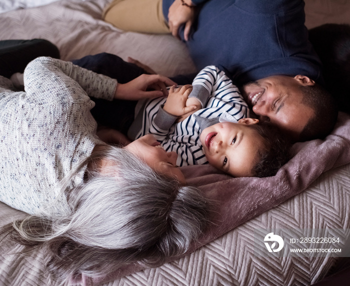 High angle portrait of happy son lying with parents on bed at home