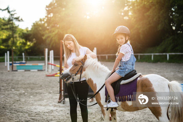 Cute little girl and her older sister enjoying with pony horse outdoors at ranch.