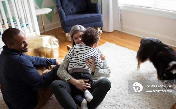 High angle view of happy father looking at mother carrying son while sitting on rug in room