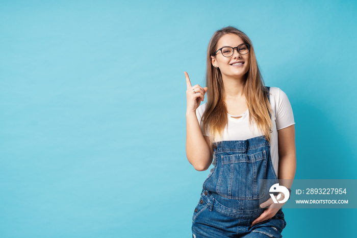 Pretty young pregnant woman pointing with the index finger up a great idea over blue background