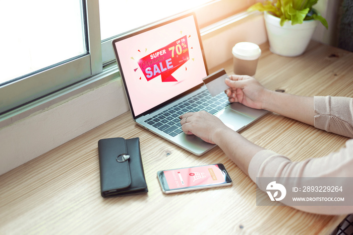 Woman using laptop computer and holding credit card on wood table near the window at home.Online sho