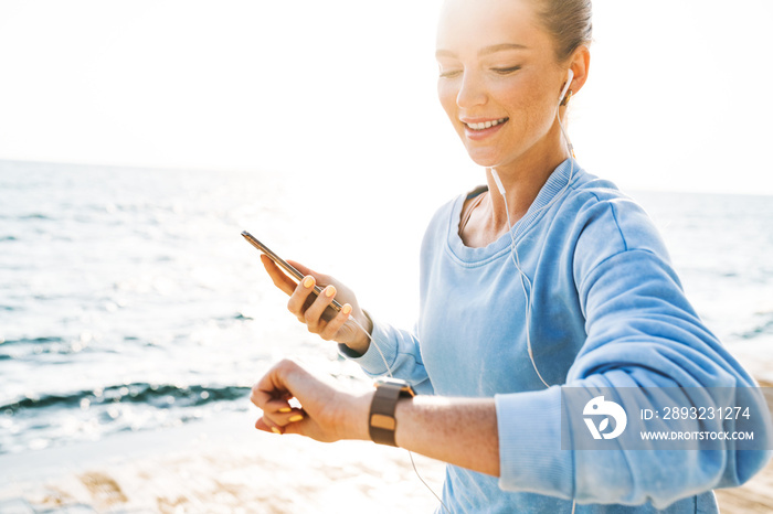 Woman running outdoors on beach looking at watch clock.