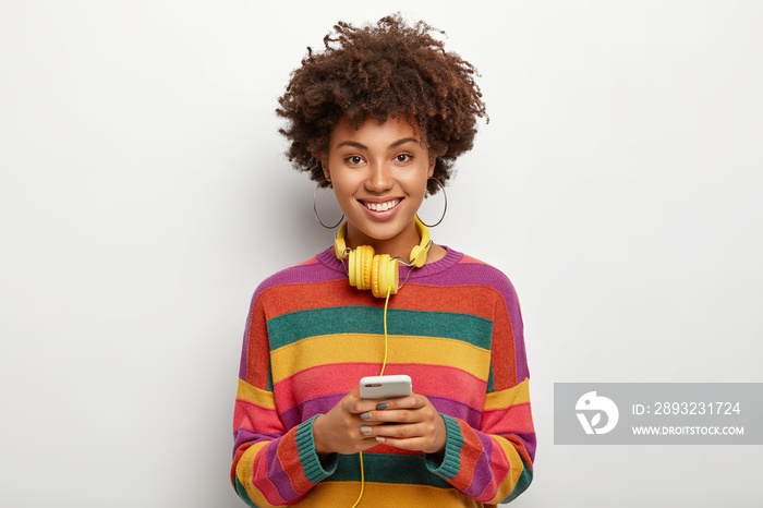 高兴的非裔美国少女拿着连接耳机的手机，听不同的音乐