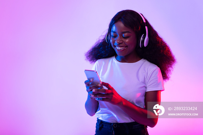 戴着无线耳机的千禧一代黑人女性在霓虹灯下使用智能手机，复制空间