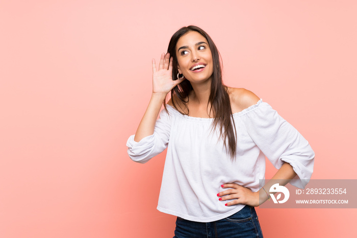 Young woman over isolated pink background listening to something by putting hand on the ear