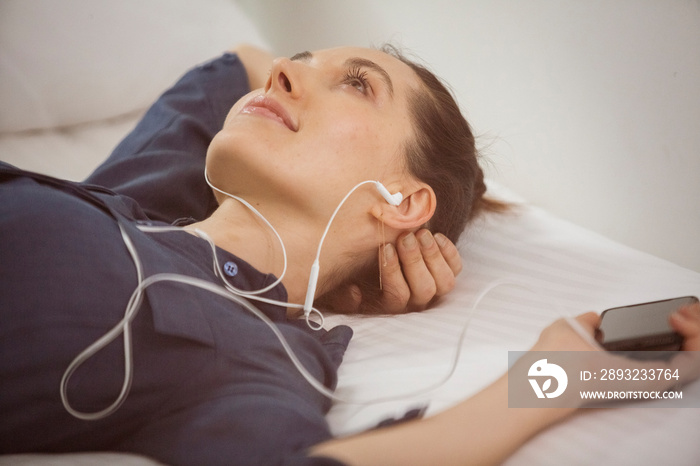 High angle view of thoughtful woman listening music while relaxing on bed at home