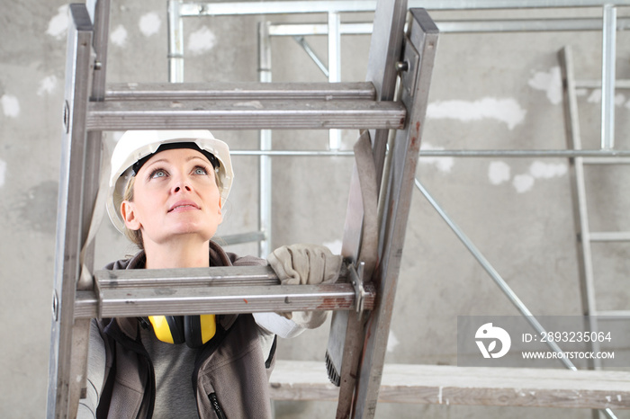 woman construction worker builder on ladder wearing white helmet and hearing protection headphones o