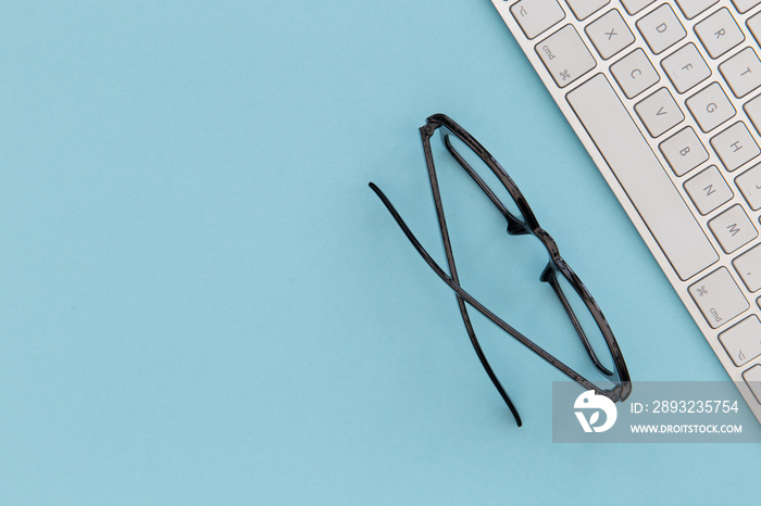 Reading glasses and computer keyboard on blue background