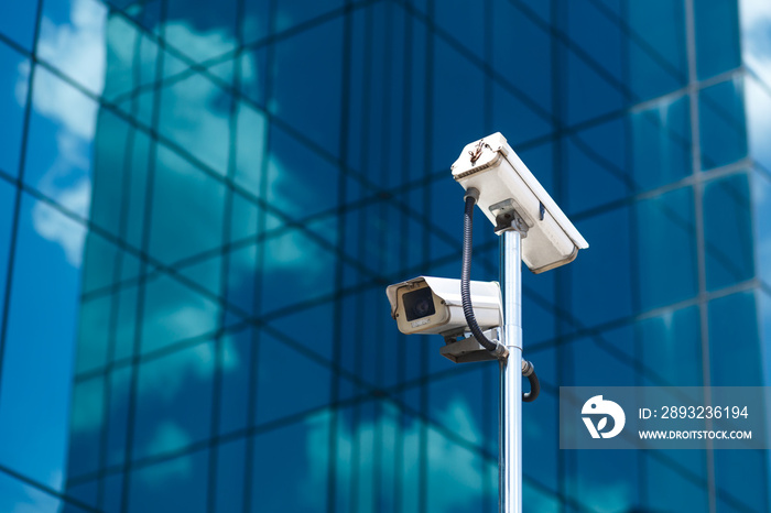 Pole with two white video surveillance cameras at big office glass building background