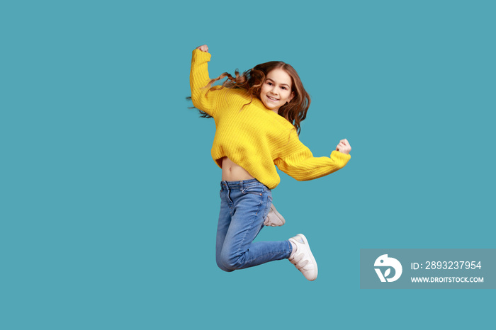 Full length portrait of little girl jumping up high, expressing happiness, celebrating success, wear
