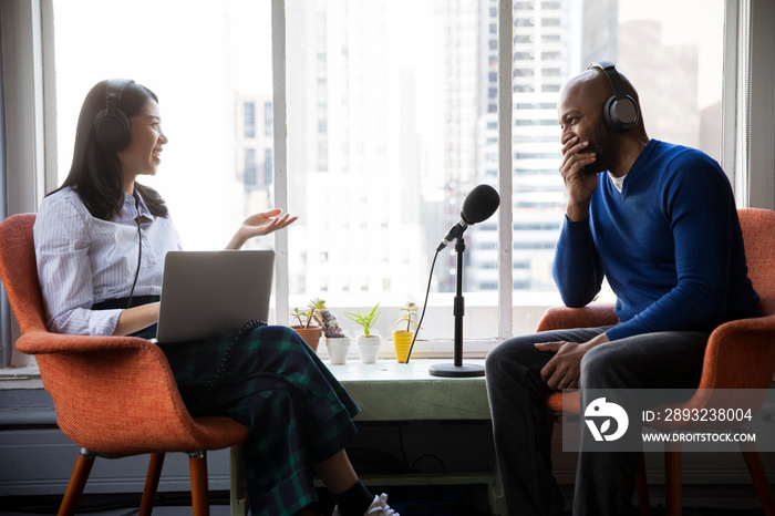 Female journalist interviewing smiling businessman while sitting on chairs by window in recording st