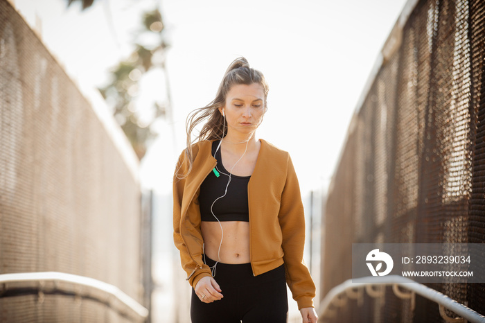 Young female athlete wearing sports clothing and jacket while listening music outdoors