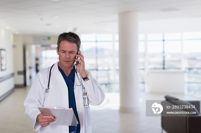 Male doctor with clipboard talking on smart phone in hospital lobby