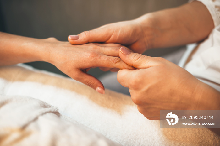 Caucasian woman having a finger massage session on hand while lying in bed at spa salon