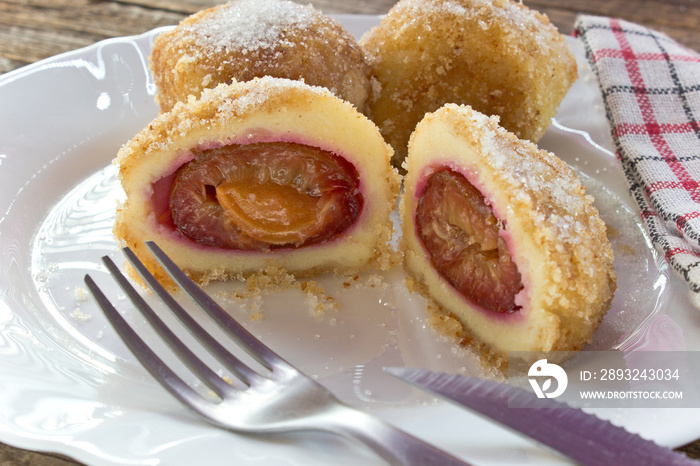 Plum dumplings on plate with fork on wooden table