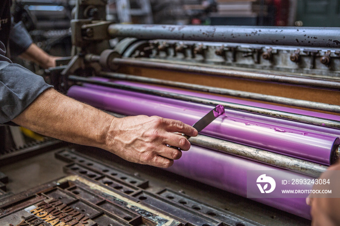 Mans hand with utility knife applying ink to printing press