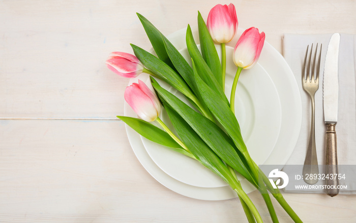 Spring table setting with pink tulips on white wooden background. Top view, copy space