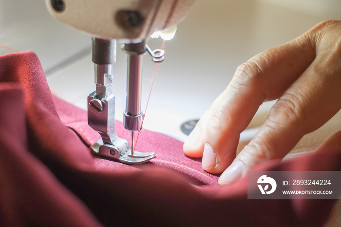 Hand of the seamstress is using a white industrial sewing machine to sew cloth.