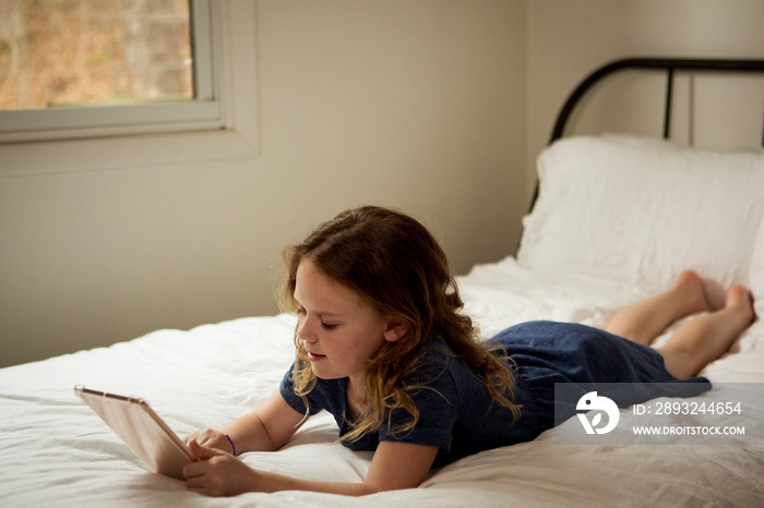 Cute girl using tablet computer while lying on bed at home