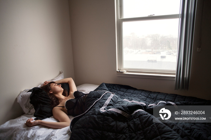 Thoughtful young woman looking out window on bed