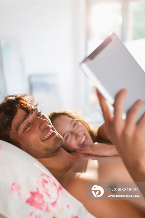 幸福的年轻夫妇在床上使用数字平板电脑
