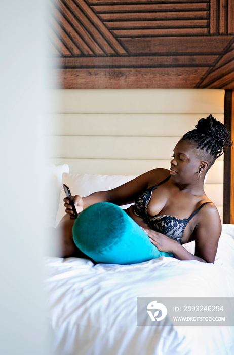 Black woman with braids laying on a blue green pillow in bed with cell phone