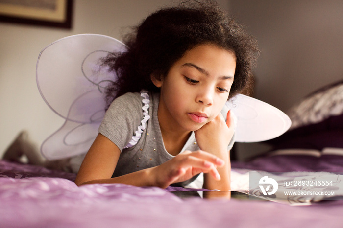 Girl with fairy wings using digital tablet on bed