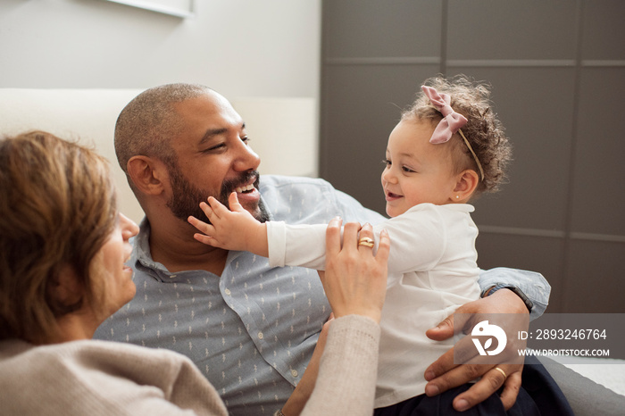 Happy parents playing with cute daughter while relaxing on bed at home