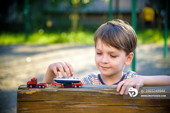 Boy plays with toy cars. Kid playing on the playground alone. Childs daytime fun