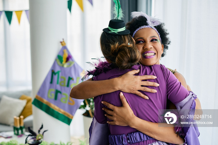 Happy female friends in carnival costumes embracing during Mardi Gras celebration festival.