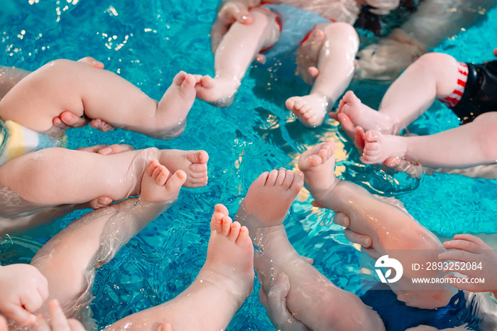 A group of mothers with their young children in a childrens swimming class with a coach.